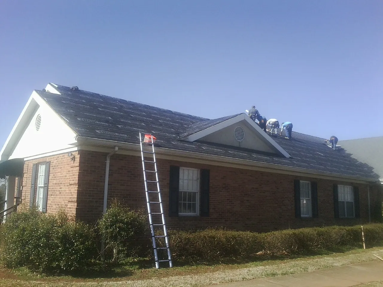 Crew tearing shingles off a brick ranch roof with a ladder set — Emergency Roof Repair work by our crew in Winston