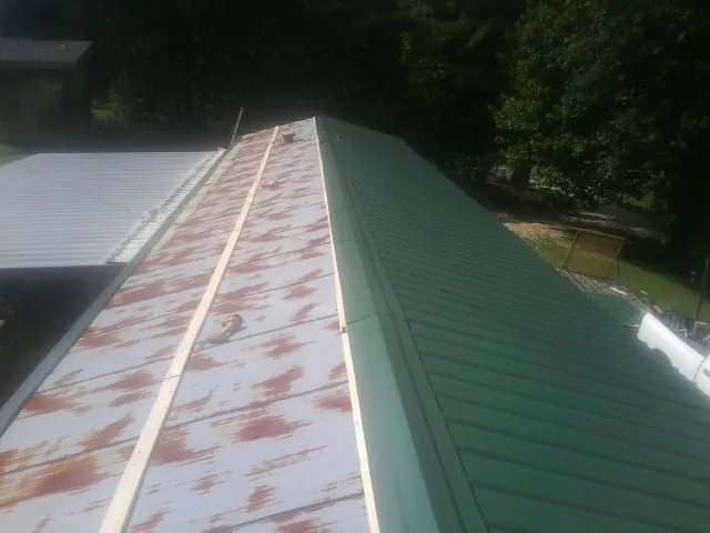 Old rusted panels beside newly installed green metal roofing — Wind Damage Roof Repair by Roofing Brothers in Winston