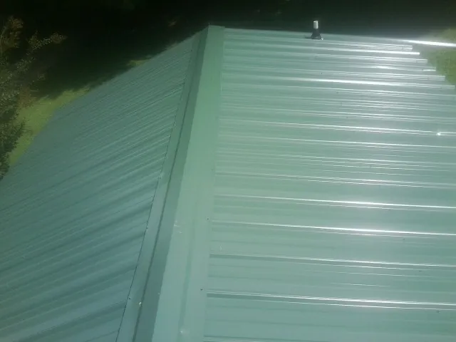 New green metal panels meeting at the ridge of a roof — Flat Roof Repair work by our crew in Winston